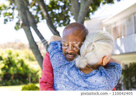 Happy diverse senior couple hugging in sunny garden Happy diverse senior couple hugging in sunny garden 110042405