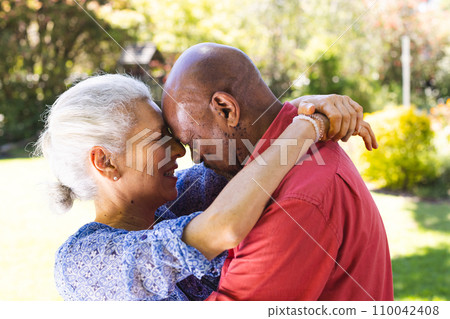 Happy diverse senior couple hugging in sunny garden Happy diverse senior couple hugging in sunny garden 110042408
