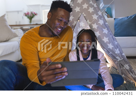Happy african american father and daughter sitting by teepee with tablet at home, copy space Happy african american father and daughter sitting by teepee with tablet at home, copy space 110042431