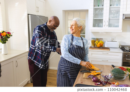Happy diverse senior couple slicing butternut squash, chopping vegetables in kitchen 110042468
