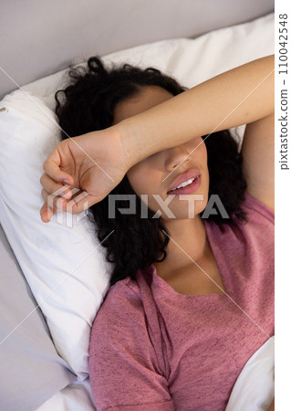 Tired biracial woman holding hand on her head resting lying in bed at sunny home Tired biracial woman holding hand on her head resting lying in bed at sunny home 110042548