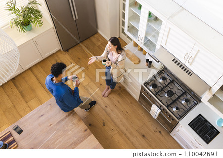 Happy diverse couple discussing and drinking tea in bright kitchen at home, copy space Happy diverse couple discussing and drinking tea in bright kitchen at home, copy space 110042691