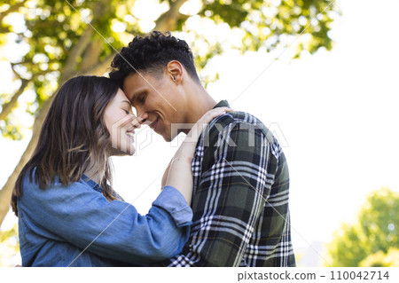 Happy diverse couple embracing and touching foreheads in sunny garden, copy space 110042714