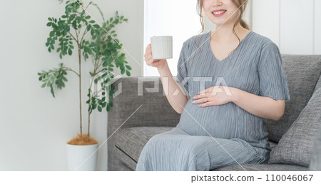 Pregnant woman/maternity/premum drinking hot drink on the sofa at home Pregnant woman/maternity/premum drinking hot drink on the sofa at home 110046067
