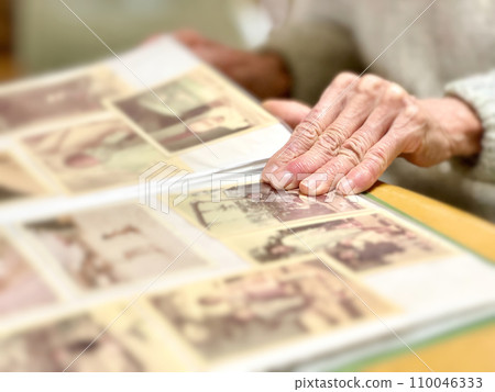 Hand of an elderly woman looking at a child's photo album Hand of an elderly woman looking at a child's photo album 110046333