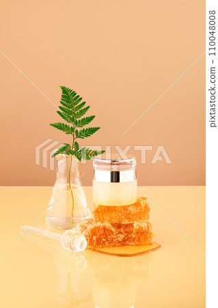 A fern leaf is inserted into an Erlenmeyer flask, a luxurious cosmetic jar placed on natural raw beeswax. Honey has the ability to stimulate collagen production, creating plumpness for the skin. A fern leaf is inserted into an Erlenmeyer flask, a luxurious cosmetic jar placed on natural raw beeswax. Honey has the ability to stimulate collagen production, creating plumpness for the skin. 110048008