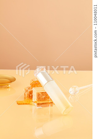 Close-up of a cosmetic bottle leaning against a glass podium with natural raw beeswax on a pastel pink background. Cosmetic mockup for advertising. Concept of natural ingredients. 110048011