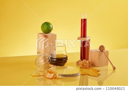 Honey fills a test tube, set against blank platforms, fresh lemons, and raw beeswax on a yellow backdrop. Embrace the healthful synergy of lemon and honey in this vibrant display. Honey fills a test tube, set against blank platforms, fresh lemons, and raw beeswax on a yellow backdrop. Embrace the healthful synergy of lemon and honey in this vibrant display. 110048021