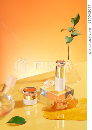 A cosmetic set with a luxurious design is displayed with glassware and honey on an orange background. Skin care concept with natural ingredients. A cosmetic set with a luxurious design is displayed with glassware and honey on an orange background. Skin care concept with natural ingredients. 110048025