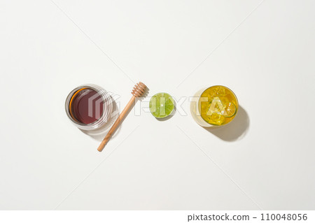 Honey in a glass jar, a honey drizzle, sliced lemon and a glass of honey kumquat tea arranged on a white background. Healthcare concept with natural products. Honey in a glass jar, a honey drizzle, sliced lemon and a glass of honey kumquat tea arranged on a white background. Healthcare concept with natural products. 110048056