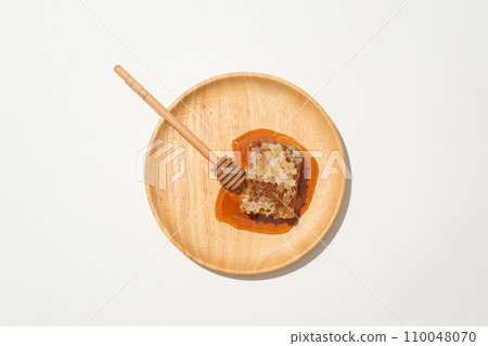 View from above of a honey drizzle and natural raw honey are displayed on wooden dish on white background. Copy space for products advertising with honey extract. 110048070