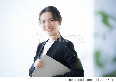 Close-up of a business woman holding a laptop looking at the camera Close-up of a business woman holding a laptop looking at the camera 110048383