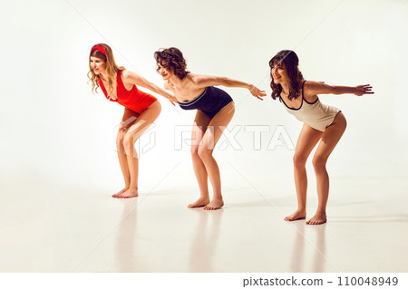 Beautiful stylish young women in vintage swimsuits standing in position to dive, swimming against white background Beautiful stylish young women in vintage swimsuits standing in position to dive, swimming against white background 110048949