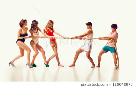 Game on. Young cheerful people, friends in swimsuits playing on beach, pulling rope against white background. Fun and joy Game on. Young cheerful people, friends in swimsuits playing on beach, pulling rope against white background. Fun and joy 110048973