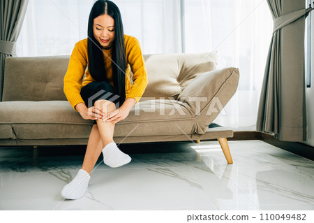 Highlighting health care concept, woman on sofa holds her injured ankle. Emphasizing varicose vein prevention leg recovery and pain relief for the patient. medical Highlighting health care concept, woman on sofa holds her injured ankle. Emphasizing varicose vein prevention leg recovery and pain relief for the patient. medical 110049482