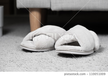 Modern grey slippers on the carpet near the sofa. Cozy and comfortable shoes for home Modern grey slippers on the carpet near the sofa. Cozy and comfortable shoes for home 110051009