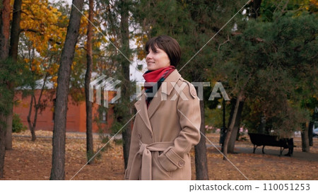 Woman with smile walks through city park to meeting with entrepreneur in autumn Woman with smile walks through city park to meeting with entrepreneur in autumn 110051253