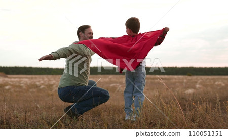 Father and son in red cape play superheroes soaring through air in imaginations Father and son in red cape play superheroes soaring through air in imaginations 110051351