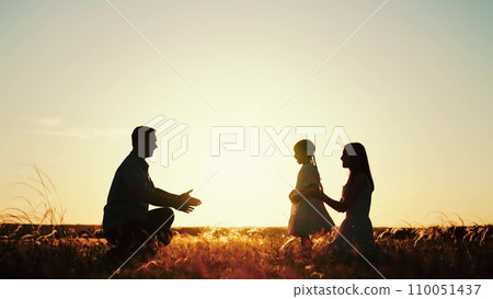 Family plays with daughter running to hugs of parents as sun sets behind rolling field 110051437