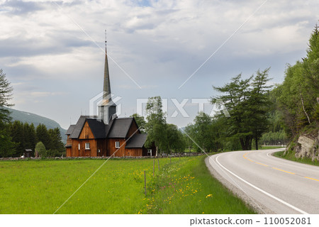 Old wooden Kvikne Kirke in Norway, surrounded by green fields and a winding road 110052081