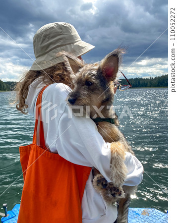 Girl with a dog in her hands is admiring the water landscape from the pier. Concept of holiday with pets 110052272
