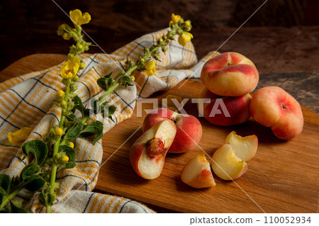 Cutting board with cut and whole saturn peaches or flat peaches on wooden background with yellow kitchen towel.. 110052934