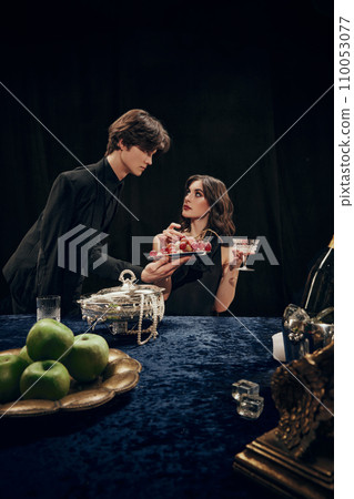 Handsome young man, waiter serving to elegant, beautiful woman plate with grapes. Luxurious dinner. Royal event Handsome young man, waiter serving to elegant, beautiful woman plate with grapes. Luxurious dinner. Royal event 110053077