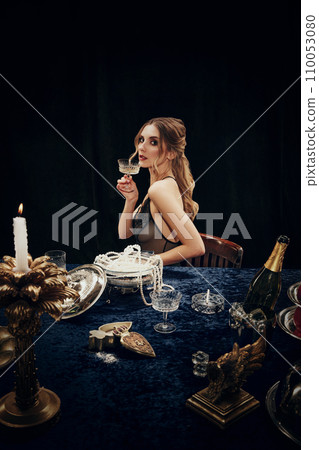 Portrait of beautiful young woman in elegant dress holding glass with champagne, attending mysterious dinner. Christmas, New Year celebration Portrait of beautiful young woman in elegant dress holding glass with champagne, attending mysterious dinner. Christmas, New Year celebration 110053080