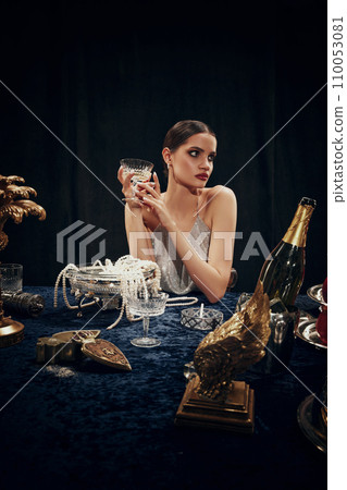 Portrait of beautiful young woman in elegant dress holding glass with champagne, attending mysterious dinner. Christmas, New Year celebration Portrait of beautiful young woman in elegant dress holding glass with champagne, attending mysterious dinner. Christmas, New Year celebration 110053081