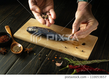 Close-up of hands adding dry pepper to Clupea fish. Concept of cooking pickled herring with spices on the kitchen table 110053657