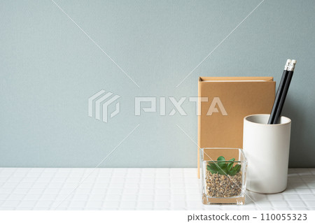 Working desk with notebook, pencil holder, potted plant on white tile desk. gray wall background Working desk with notebook, pencil holder, potted plant on white tile desk. gray wall background 110055323