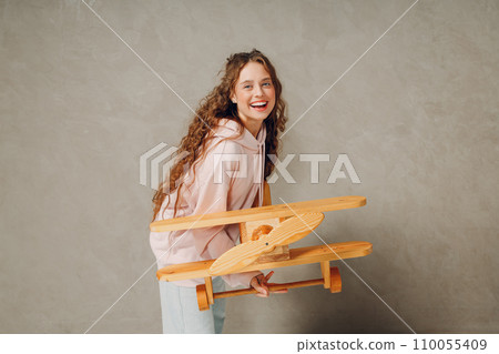 Happy young woman smiles and holding a toy wooden airplane on a gray background 110055409