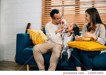 A delightful family enjoys TV and popcorn on grooved sofa fostering moments of togetherness and bonding. father mother daughter and sibling share laughter epitomizing genuine family happiness. A delightful family enjoys TV and popcorn on grooved sofa fostering moments of togetherness and bonding. father mother daughter and sibling share laughter epitomizing genuine family happiness. 110055443