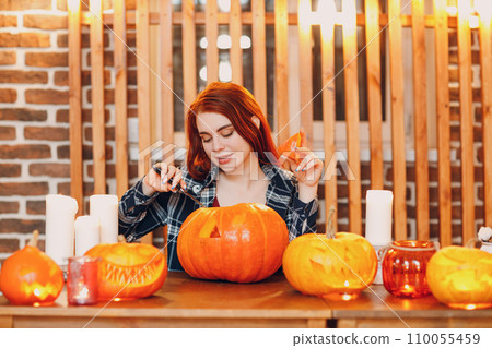 Young woman making Halloween pumpkin Jack-o-lantern. Female hands cutting pumpkins with knife 110055459