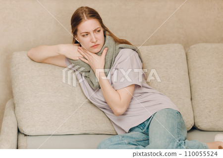 Young woman wearing scarf has flu ill sick disease cold at home indoor on sofa Young woman wearing scarf has flu ill sick disease cold at home indoor on sofa 110055524