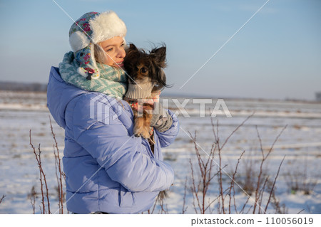 The woman has to keep her dog warm by putting the animal under her jacket. The woman has to keep her dog warm by putting the animal under her jacket. 110056019