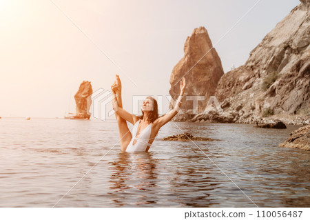 Woman sea fitness. Happy woman in a white bikini performing pilates in the sea on the beach. Female fitness yoga routine concept. Healthy lifestyle. 110056487