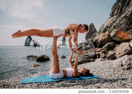 Woman sea yoga. Two Happy women meditating in yoga pose on the beach, ocean and rock mountains. Motivation and inspirational fit and exercising. Healthy lifestyle outdoors in nature, fitness concept. 110056508