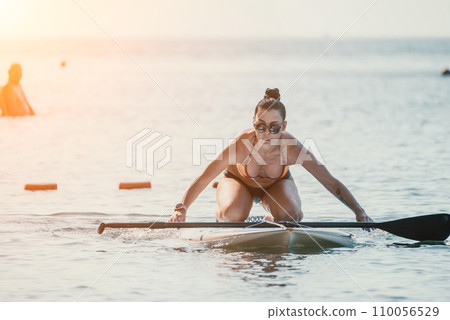 Sea woman sup. Silhouette of happy middle aged tanned woman in rainbow bikini, surfing on SUP board, confident paddling through water surface. Idyllic sunset. Active lifestyle at sea or river. Sea woman sup. Silhouette of happy middle aged tanned woman in rainbow bikini, surfing on SUP board, confident paddling through water surface. Idyllic sunset. Active lifestyle at sea or river. 110056529