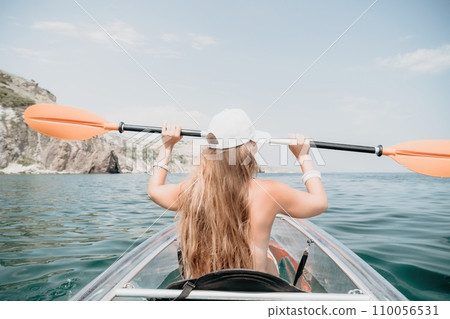 Woman in kayak back view. Happy young woman with long hair floating in transparent kayak on the crystal clear sea. Summer holiday vacation and cheerful female people relaxing having fun on the boat 110056531