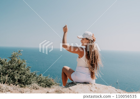 Woman summer travel sea. Happy tourist enjoy taking picture outdoors for memories. Woman traveler posing over sea bay surrounded by volcanic mountains, sharing travel adventure journey 110056535