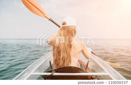 Woman in kayak back view. Happy young woman with long hair floating in transparent kayak on the crystal clear sea. Summer holiday vacation and cheerful female people relaxing having fun on the boat Woman in kayak back view. Happy young woman with long hair floating in transparent kayak on the crystal clear sea. Summer holiday vacation and cheerful female people relaxing having fun on the boat 110056537