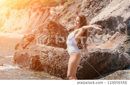 Woman travel sea. Happy tourist in white bikini enjoy taking picture outdoors for memories. Woman traveler posing on the beach at sea surrounded by volcanic mountains, sharing travel adventure journey 110056588