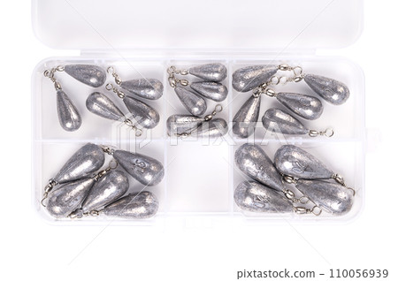 Box with fishing pear lead set. Plastic box filled with six different pear-shaped lead weights for fishing, from 5 to 20 grams, fused with wire and eyelets. Isolated, from above, over white. Photo. 110056939