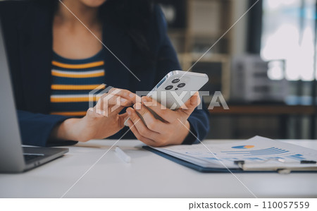 Charming Young asian businesswoman sitting on laptop computer in the office, making report calculating balance Internal Revenue Service checking document. 110057559
