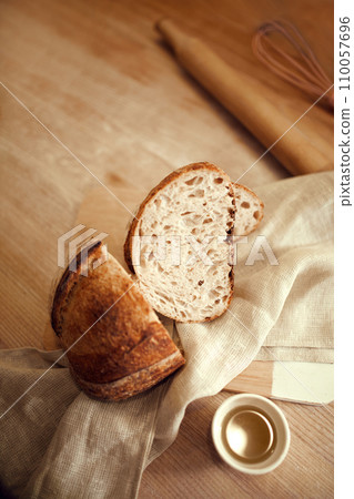 Pieces of just prepared, delicious, hot homemade loaf of bread with golden brown crispy crust lying in natural fabric on wooden table with honey in small plate. Pieces of just prepared, delicious, hot homemade loaf of bread with golden brown crispy crust lying in natural fabric on wooden table with honey in small plate. 110057696