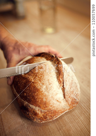 Bakery man, chef cut on wooden cutting board just prepared, delicious, hot loaf of bread with golden brown crispy crust. Concept of bakery shop 110057699