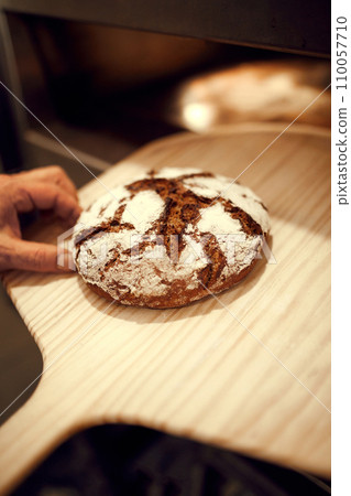 Close up shot of unrecognizable baker taken out of oven hot and tasty loaf of bread with special bread shovel. Concept of traditional recipes. 110057710
