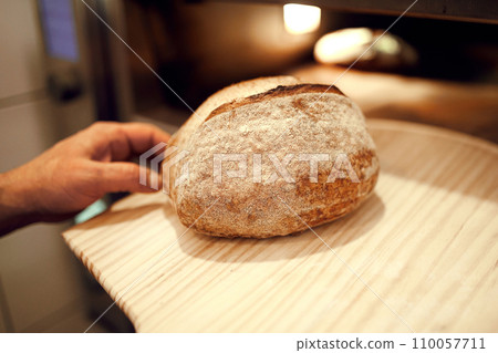 Unrecognizable baker taken out of oven hot and tasty loaf of bread with special bread shovel. Concept of traditional recipes. 110057711