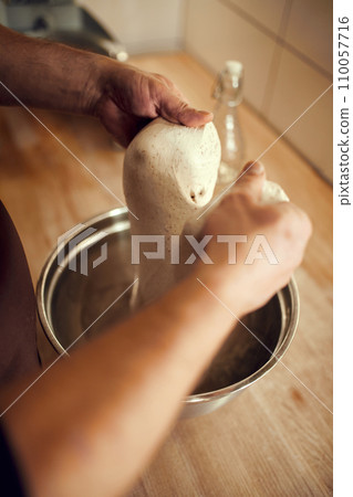 Person using their hands to push and fold dough over and over again for high-quality and soft baked goods. pastry white and slightly sticky. 110057716